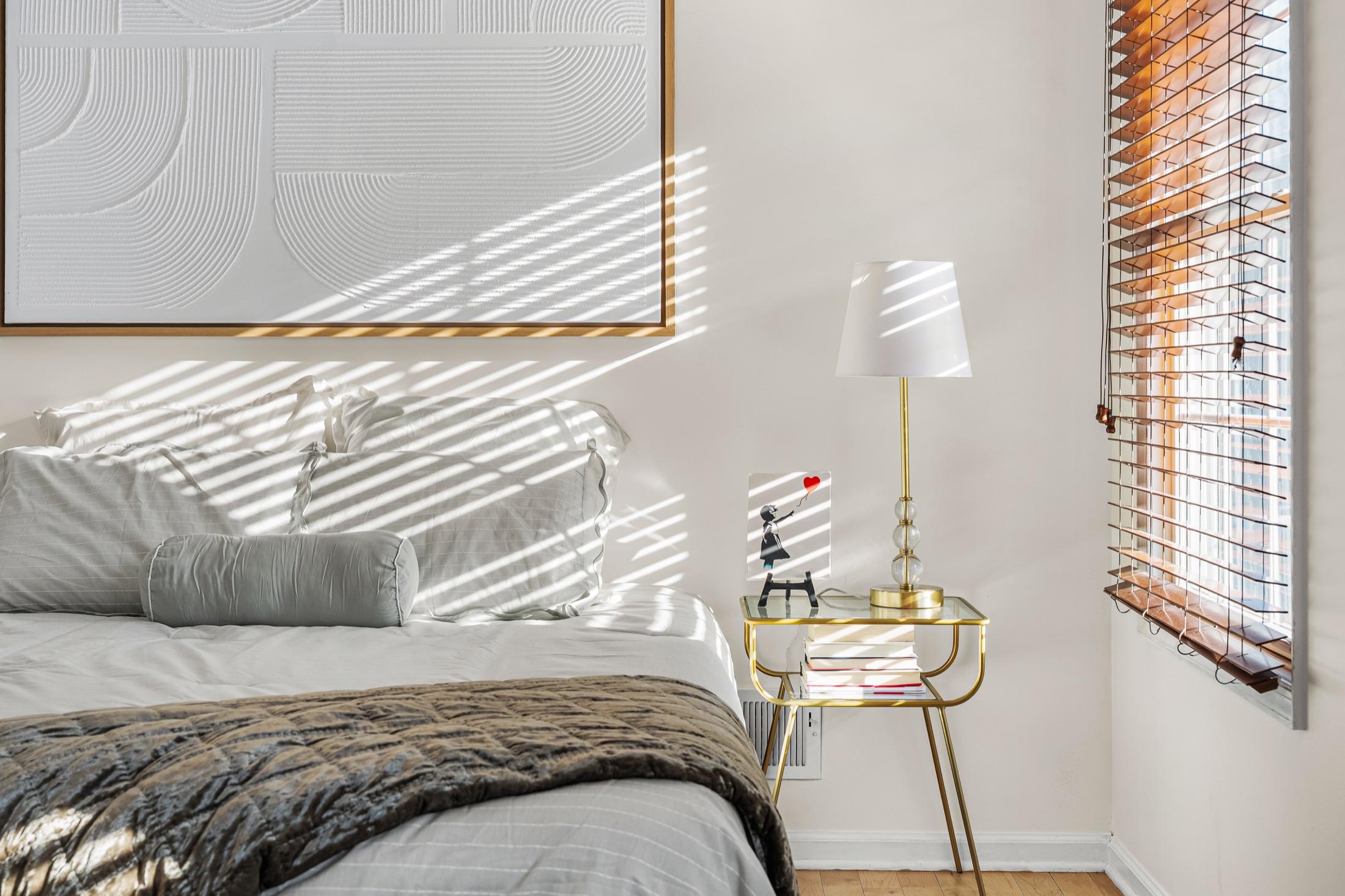 Bedroom detail with morning light streaming through wood blinds across the bedding