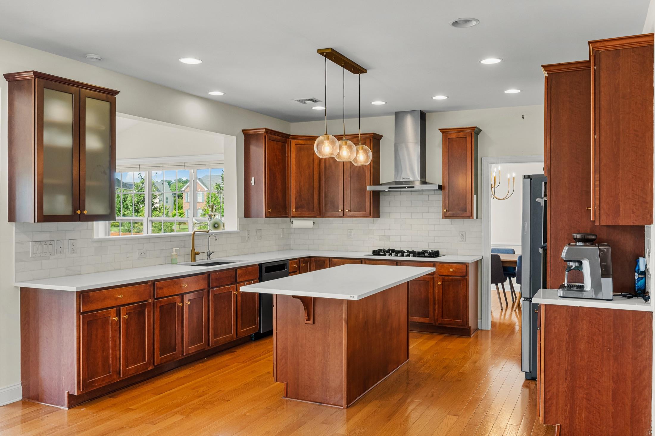 Cherry-cabinet kitchen with quartz island, marble subway backsplash & brass pendant lighting
