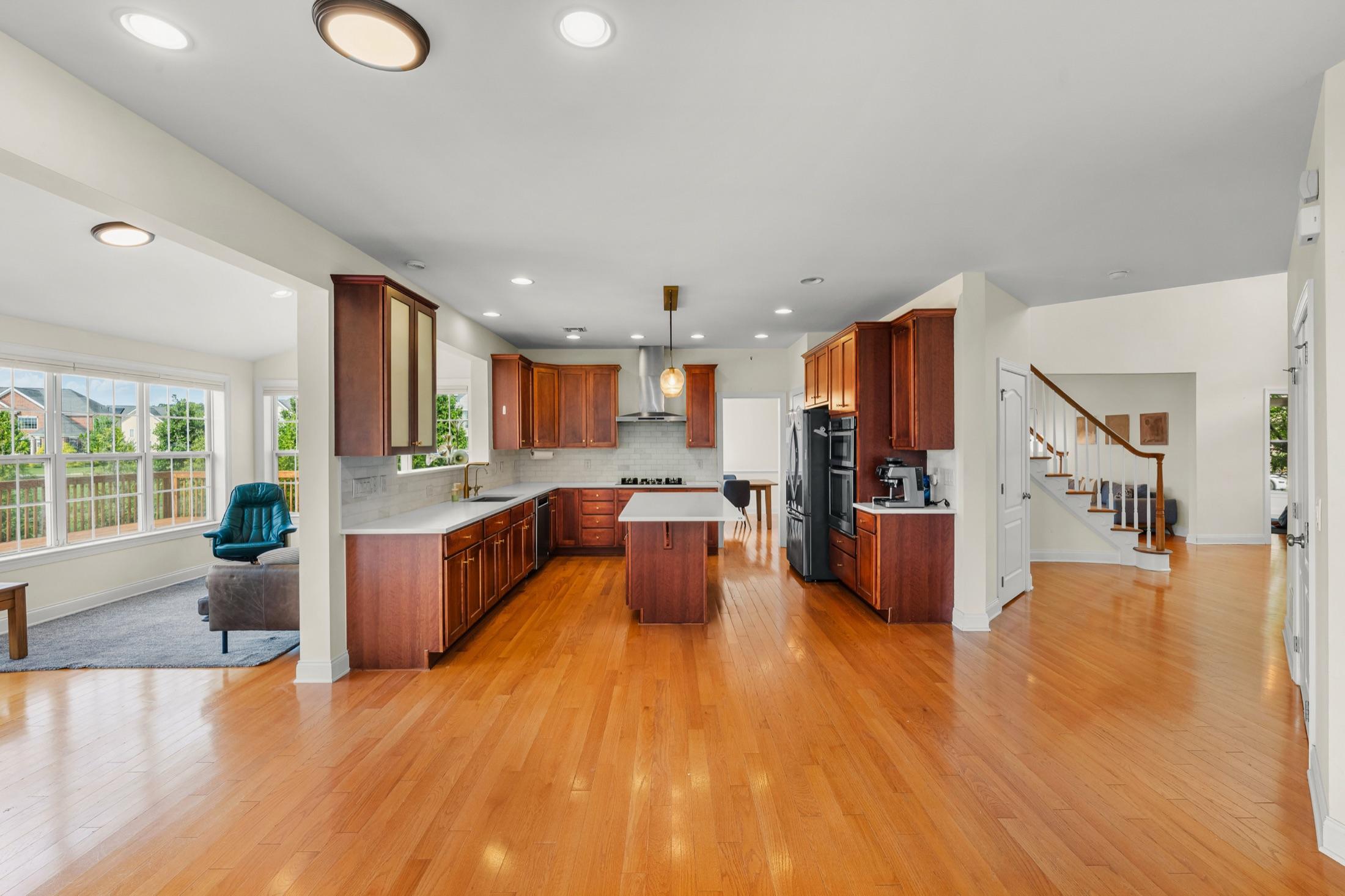 Sunlit open-concept main floor with hardwood floors, kitchen island & staircase