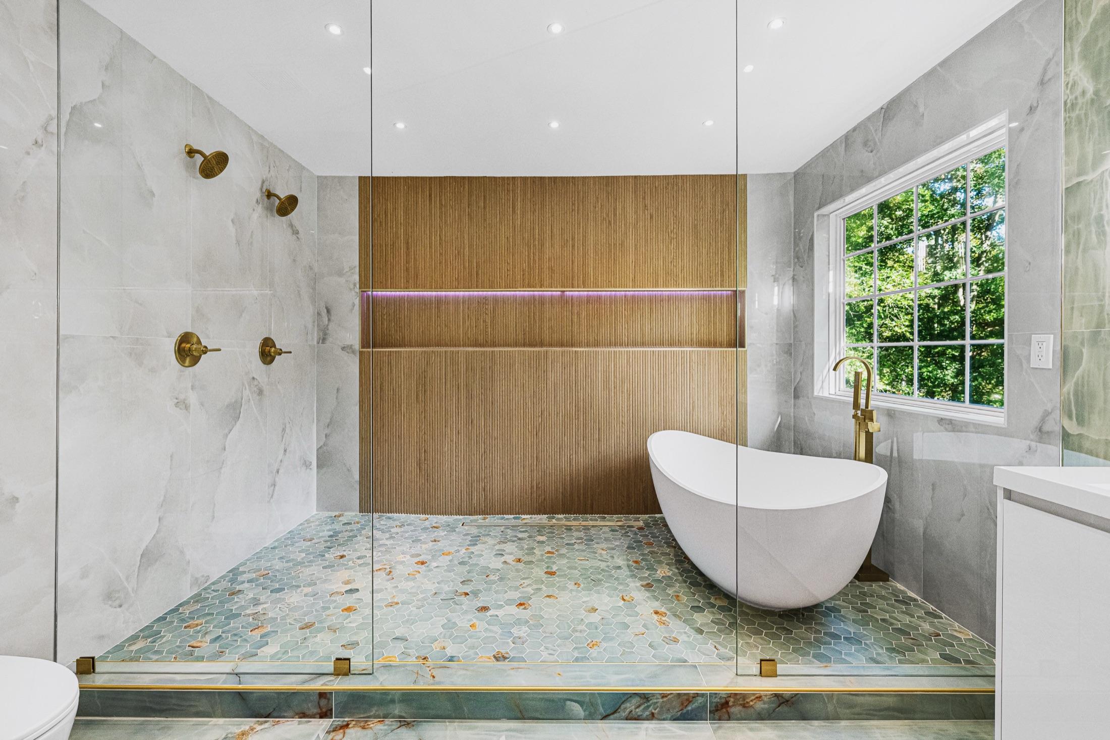 Spa-style primary bathroom with double rain shower, freestanding tub, fluted wood accent wall & onyx mosaic floor