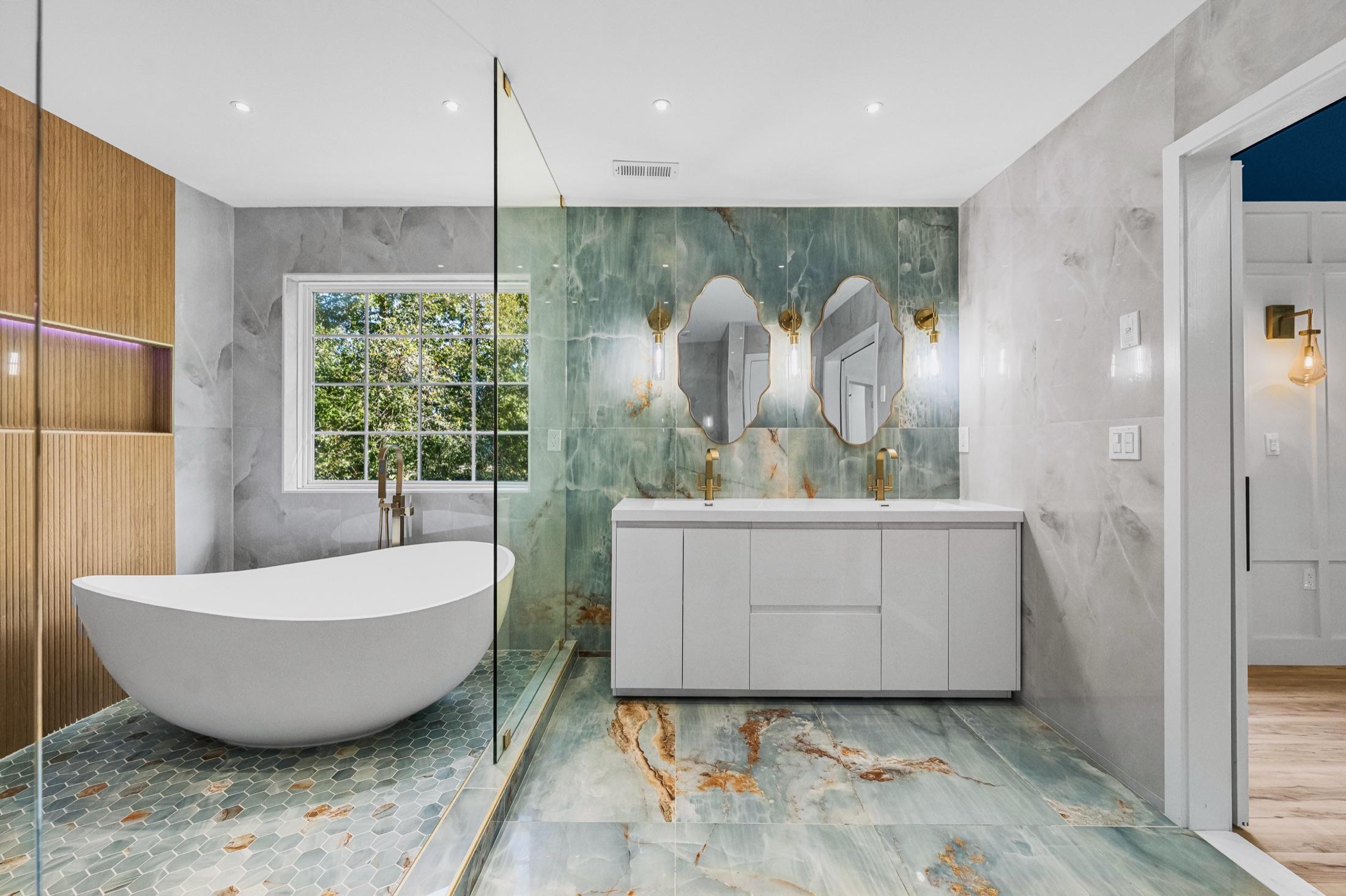 Luxury primary bathroom with green onyx tile, double vanity, brass fixtures & freestanding tub