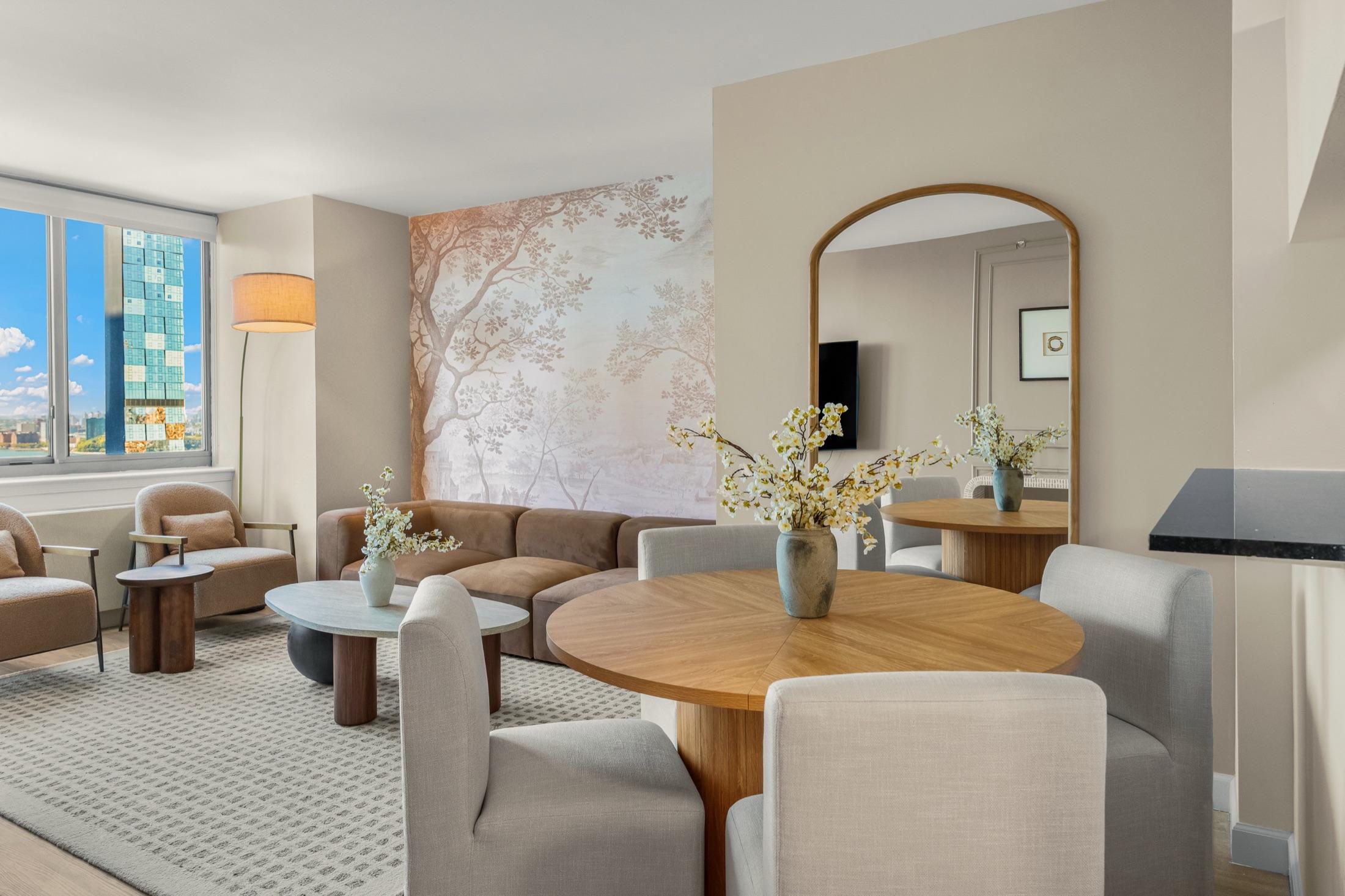 Open living and dining area with a tree mural wall, arched mirror, and Hudson River glimpse, Manhattan short-term rental