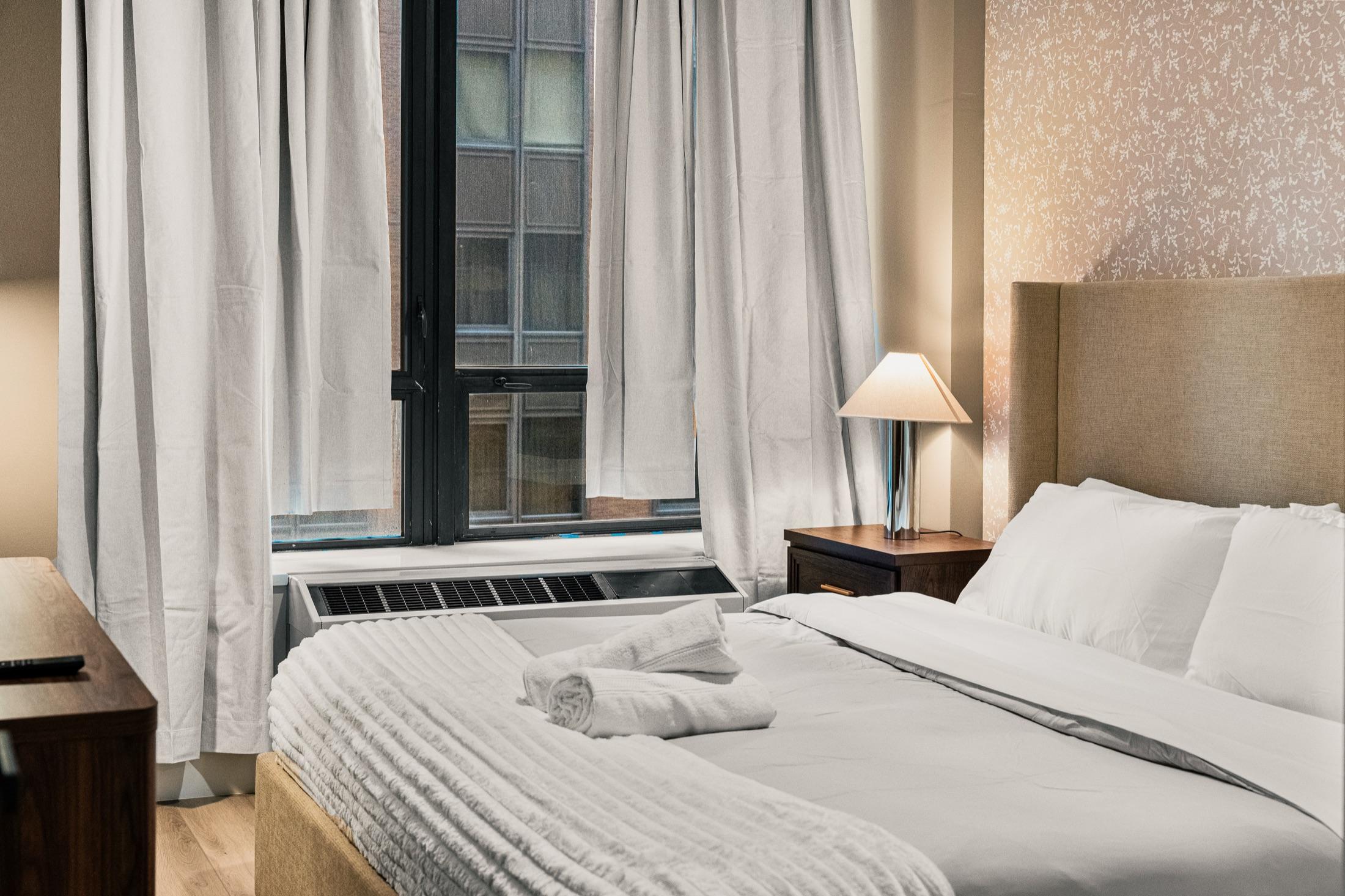 Hotel-style bedroom with upholstered headboard and folded towels, Manhattan short-term rental apartment
